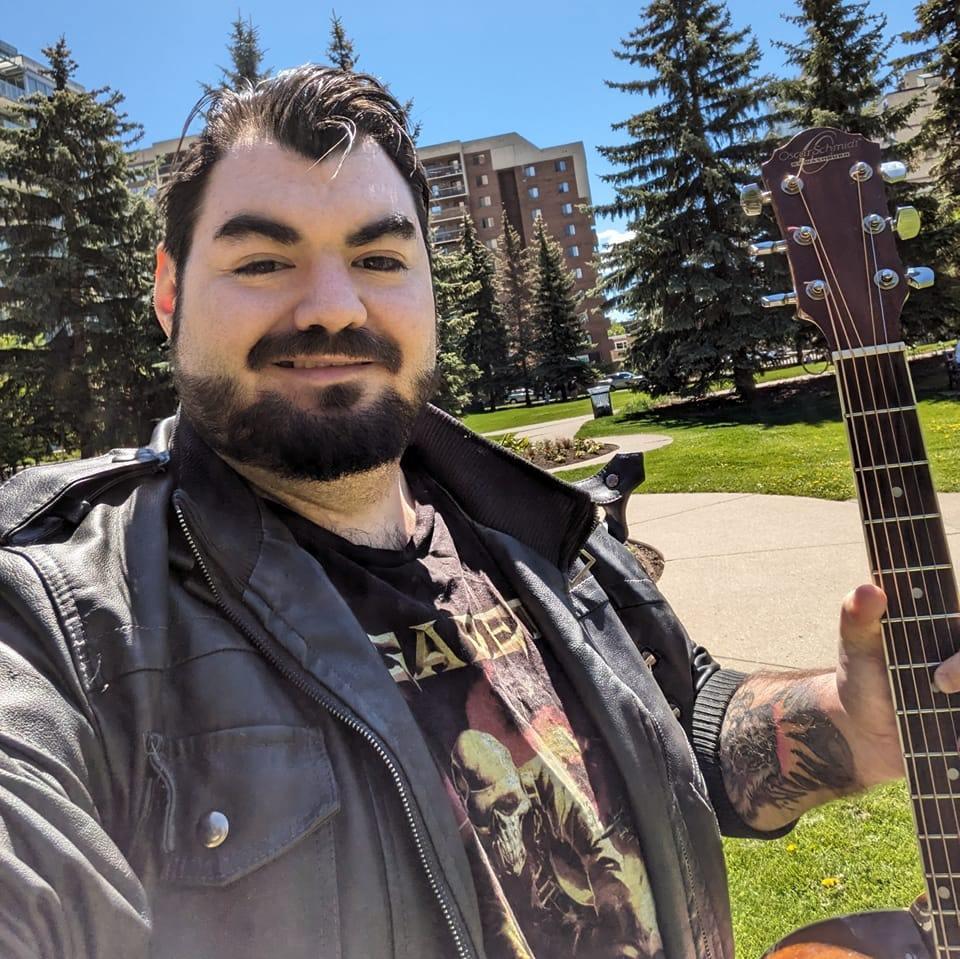 Paul Elliott Messier smiling in the sun with an acoustic guitar